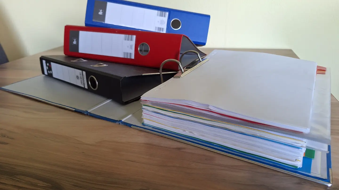 mehrere Ordner auf dem Schreibtisch,
 einer davon geöffnet